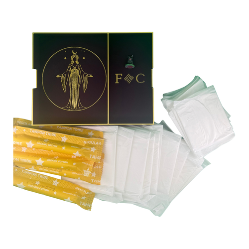 The Fortune Coochi box standing open, gold goddess emblem and F C monogram on the lid, with gold-wrapped organic tampons, pads and liners fanned out in front.